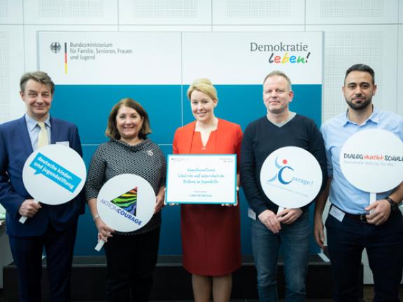 5 Personen, die alle ein Schild für ihre Organisation in der Hand halten - alle 5 Partner_innen des Kompetenznetzwerkes