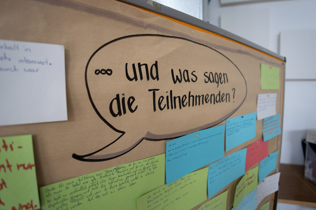 Eine Pinnwand mit der Überschrift: Und was sagen die Teilnehmenden. Darunter hängen Karten mit handschriftlichen Aussagen von Teilnehmenden.