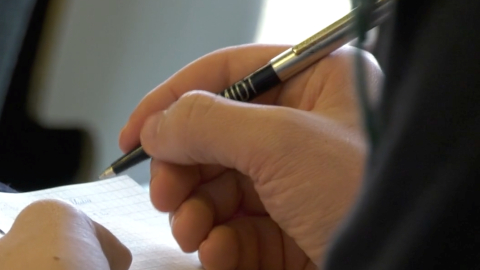 Eine Hand, die einen Kuli hält und etwas in ein Notizbuch schreibt