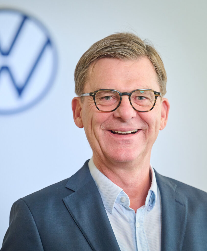 Foto von Prof. Thomas Edig, Geschäftsführer 
Personal & Organisation, Volkswa-gen Sachsen GmbH im Anzug. Mann mit Brille, der in die Kamera lacht.
