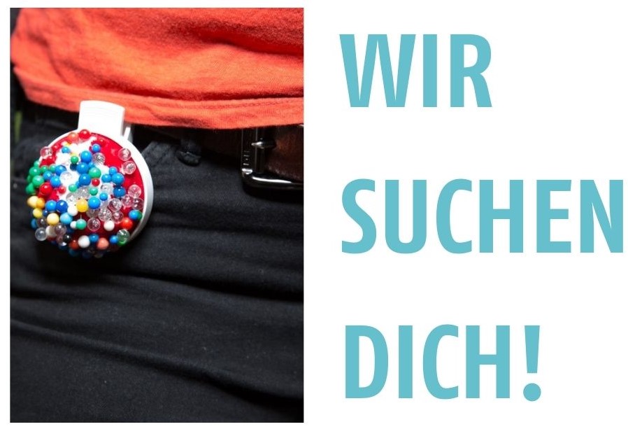 An einer Hose ist ein angeklemmtes Pinnnadelkissen zu sehen. Auf dem Bild steht: Wir suchen dich!