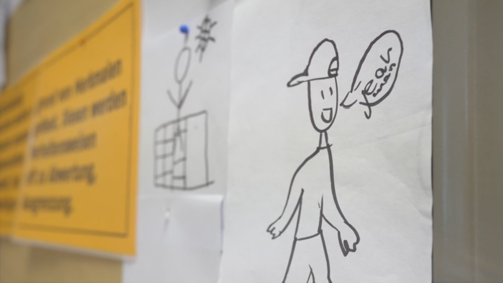 Pinnwand mit Schrift und Zeichungen, im Vordergrund eine Comicfigur mit der Sprechblase "jeah man"