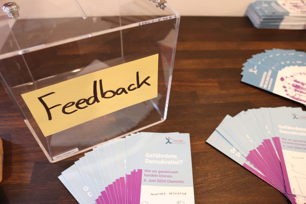 Eine Box mit Schlitz mit der Aufschrift Feedback steht auf einem Tisch, auf dem auch Flyer liegen zum Fachtag