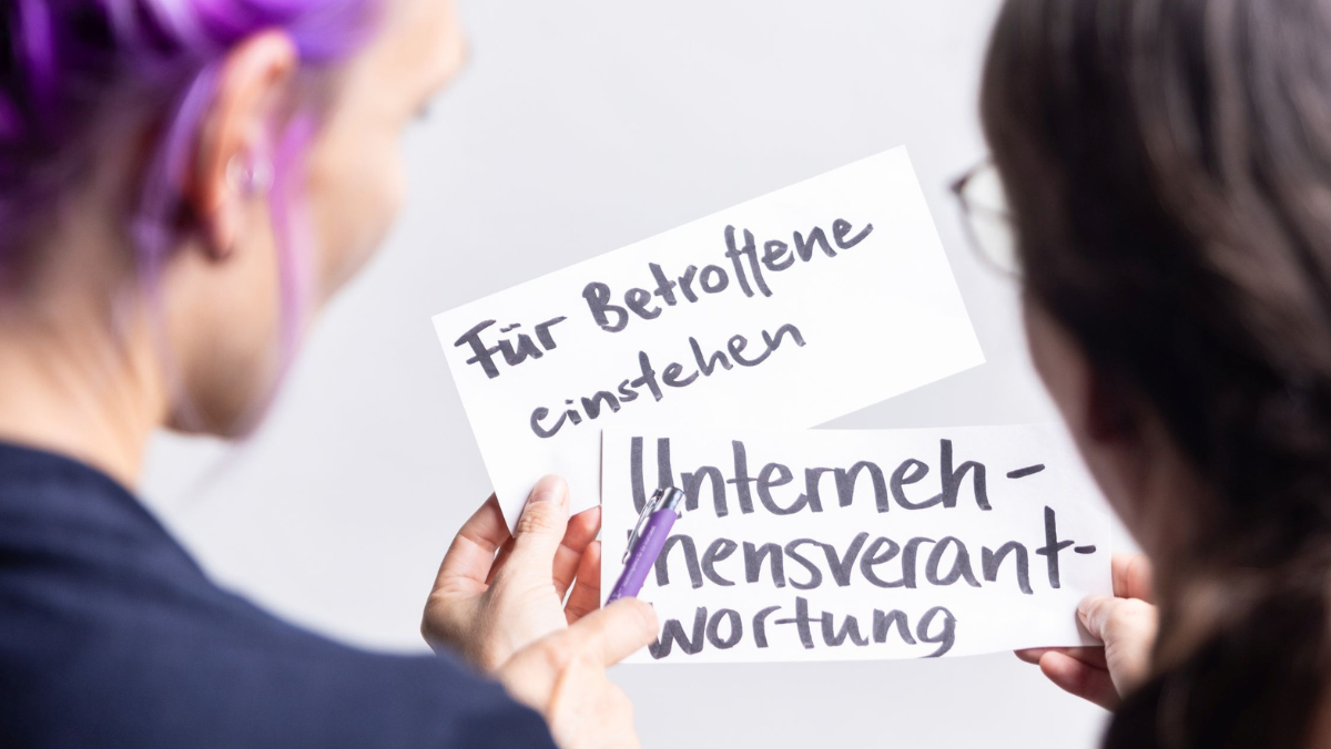 Zwei Personen haben zwei Moderationskarten in der Hand mit den Aufschriften "Für Betroffene einstehen" und "Unternehmensverantwortung"