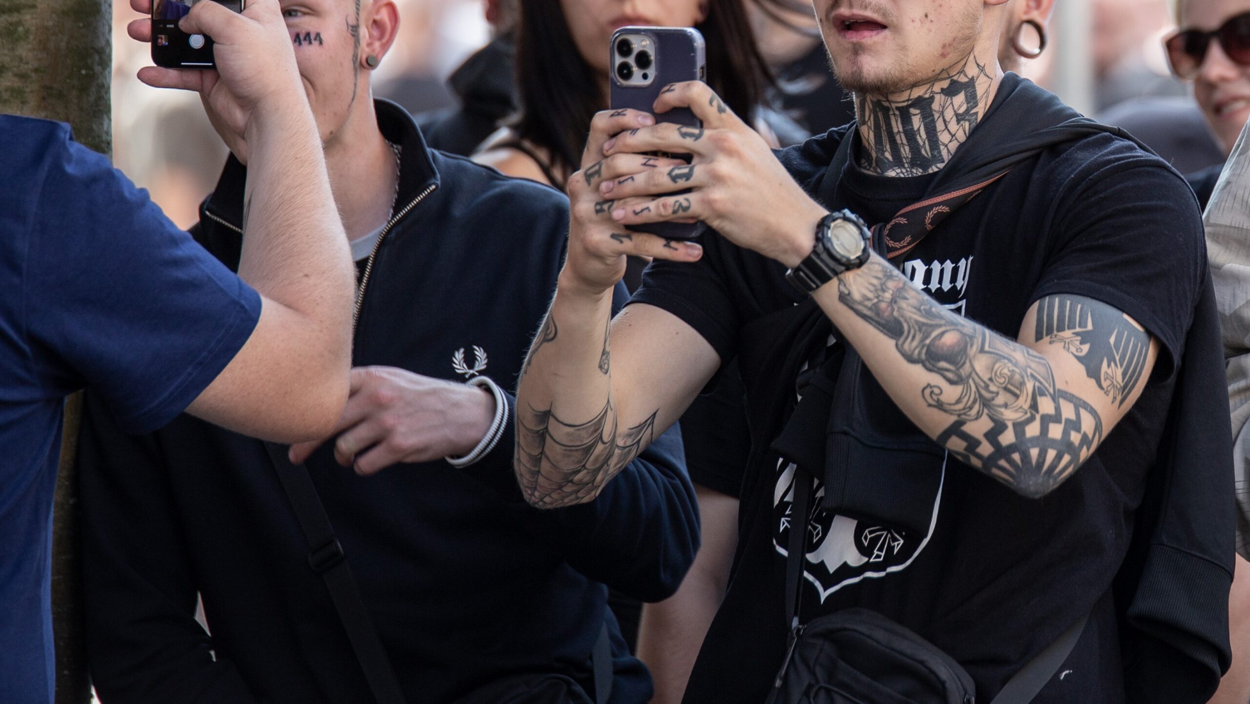 Ausschnitt aus einer Menschenmenge mit 3 Personen der extremen Rechten mit Tattoos und Handys
