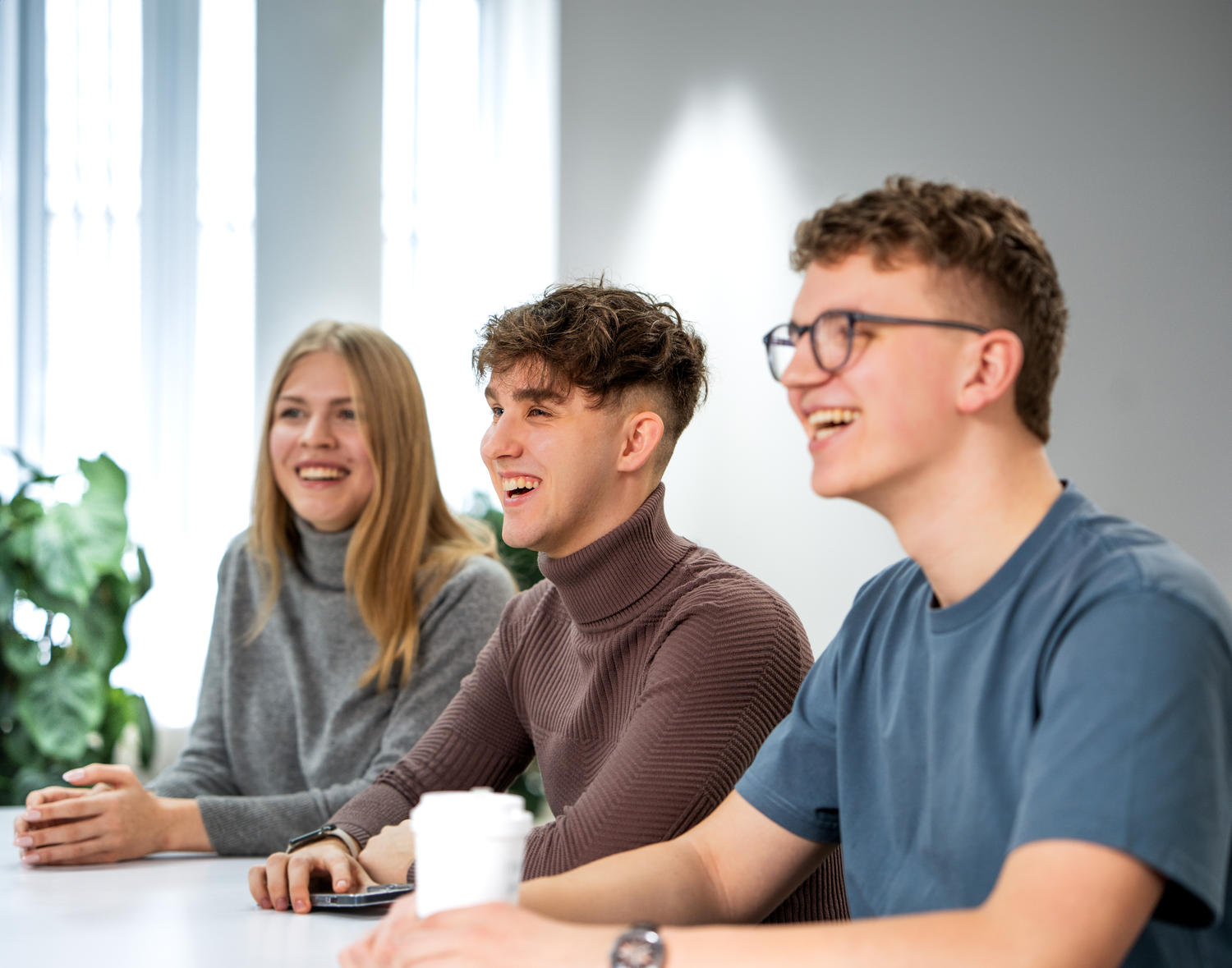 3 Personen sitzen am Tisch und lächeln