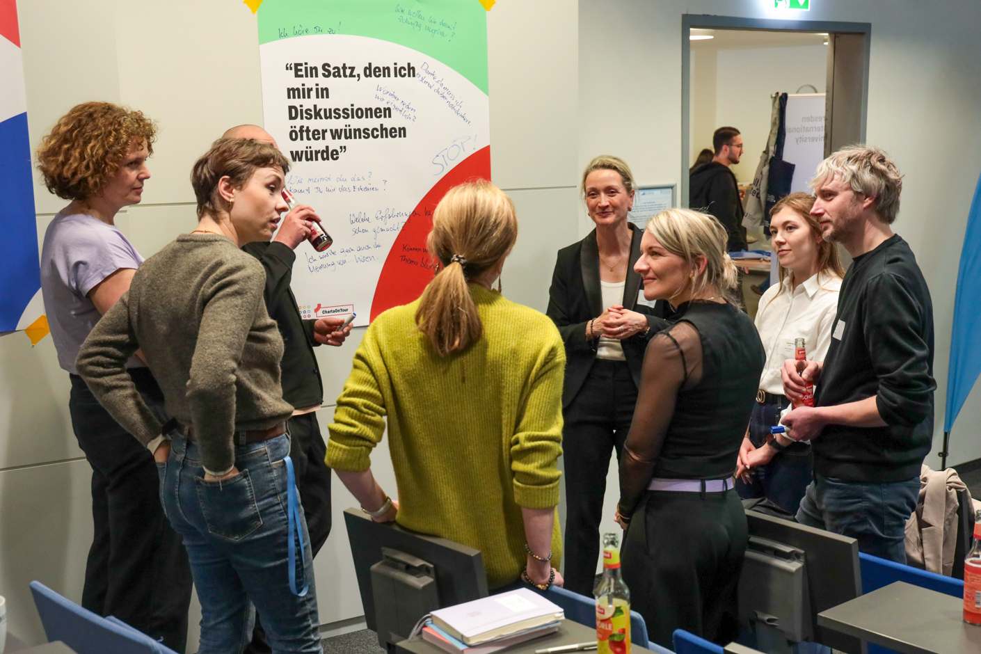 Acht Teilnehmende, die im Halbkreis stehen und miteinander diskutieren.