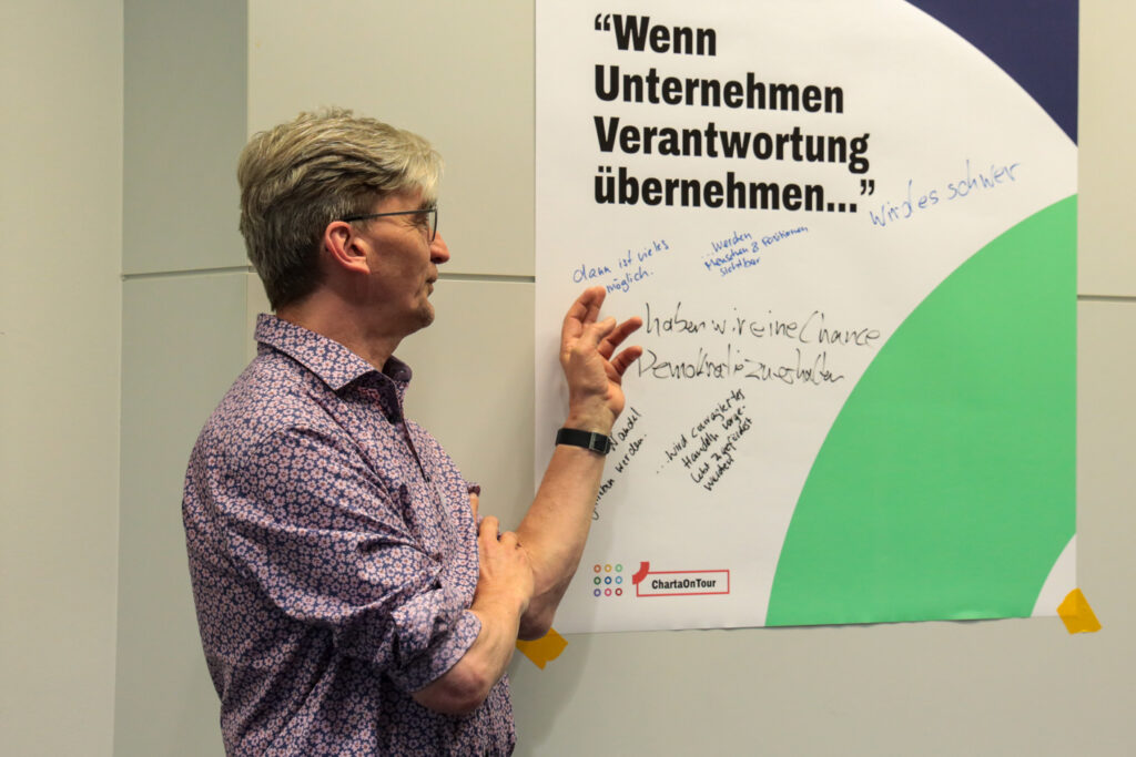 Person erklärt etwas an einem Plakat, das betitelt ist mit: "Wenn Unternehmen Verantwortung übernehmen..."