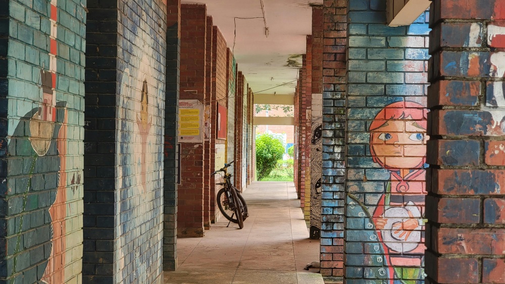 Säulengang vor einem Schulgebäude mit Graffiti an den Wänden, in der Mitte lehnt ein Fahrrad.