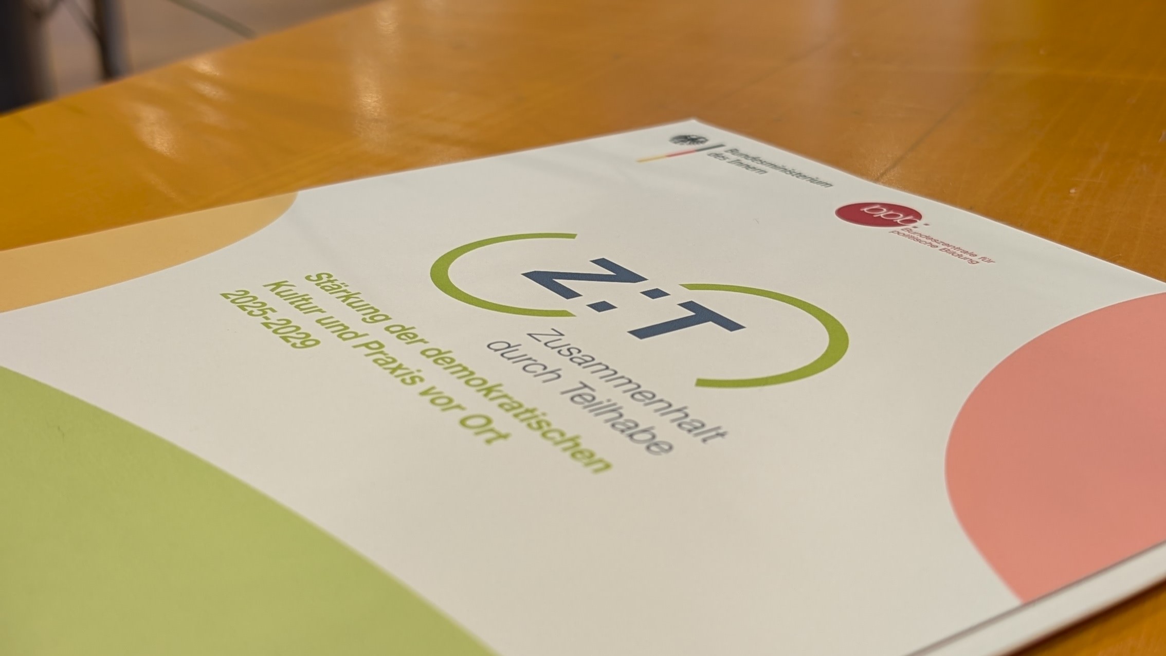 Auf einem Tisch liegt eine Mappe mit dem Aufdruck Z:T Zusammenhalt durch Teilhabe, Stärkung der demokratischen Kultur und Praxis vor Ort 2025 bis 2029